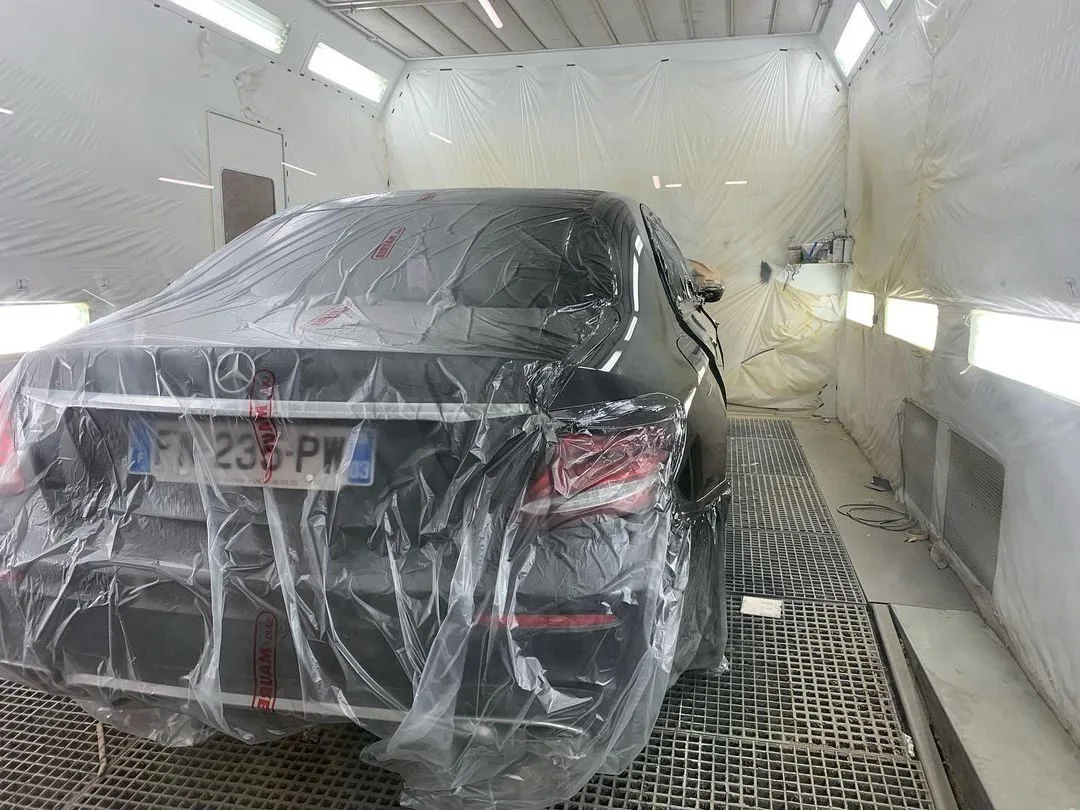 Berline protégée par une bâche dans la cabine de peinture